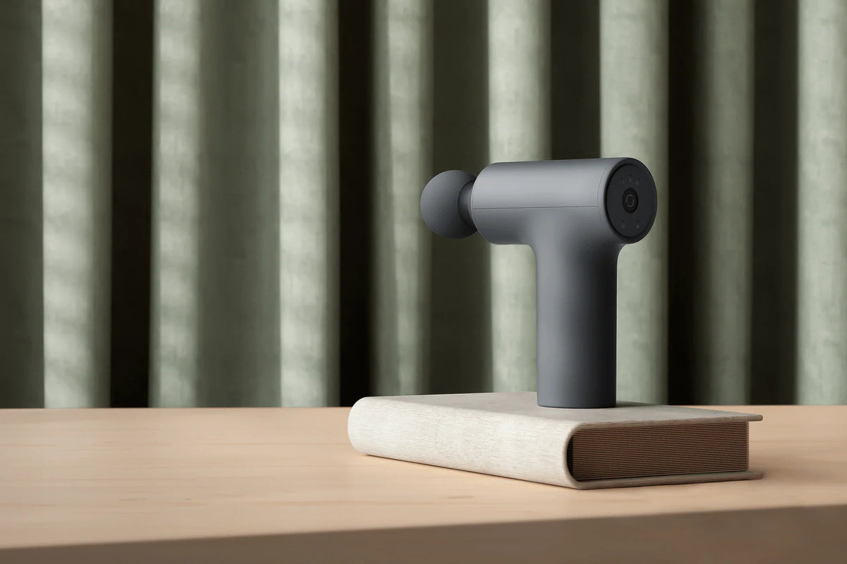 Xiaomi Massage Gun Mini 2 op een boek op een houten tafel