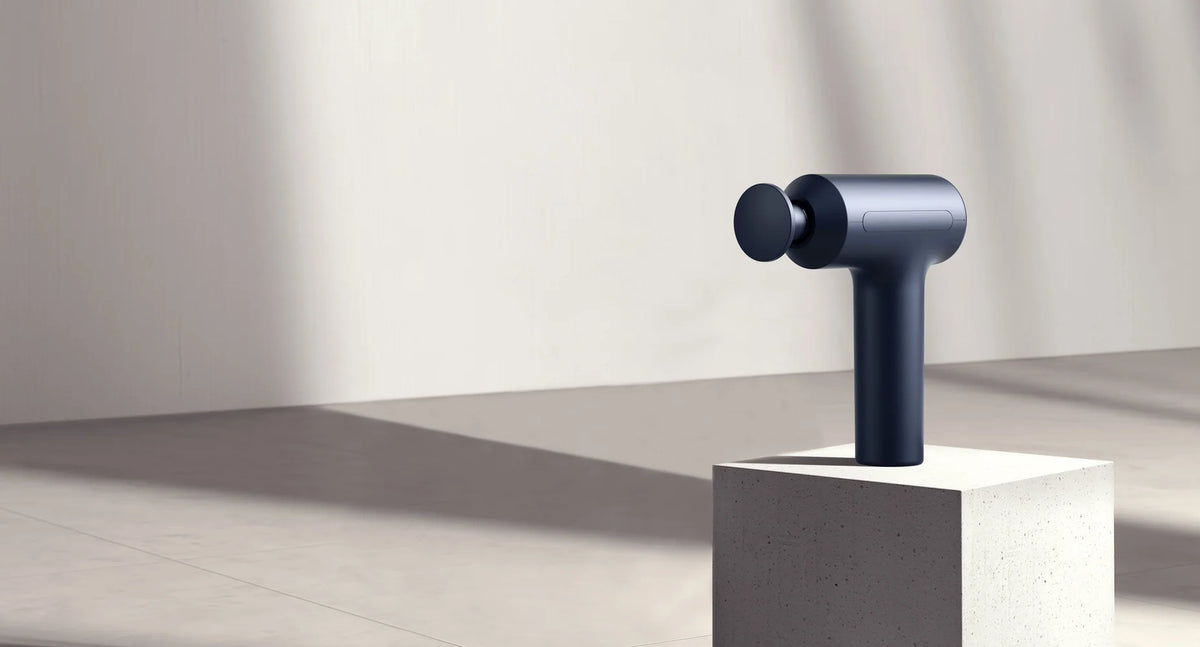 Xiaomi Massage Gun 2 op een witte sokkel in zacht zonlicht