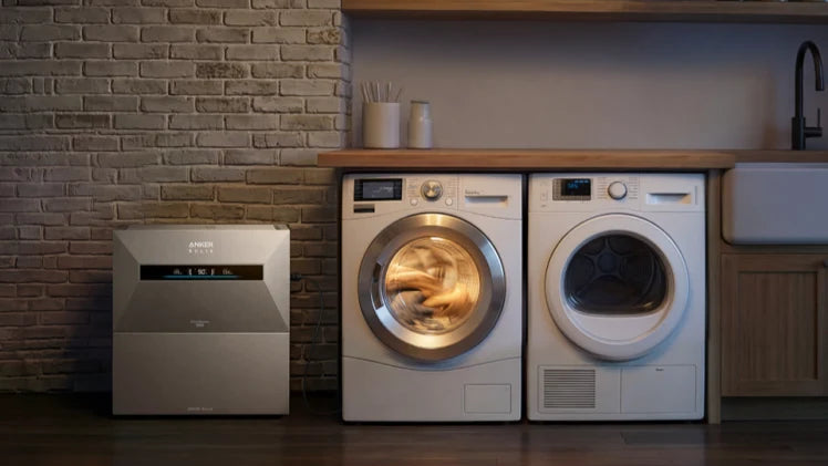 Anker SOLIX Solarbank Max AC in een wasruimte die opgeslagen zonne-energie levert aan huishoudelijke apparaten zoals een wasmachine en droger.