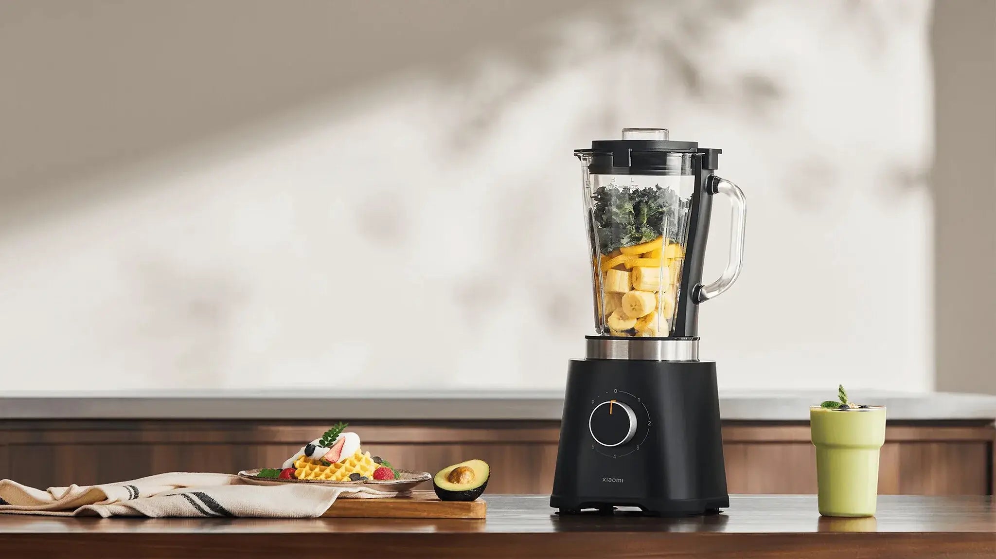 Zwarte Xiaomi blender met bananen, spinazie en ingrediënten omgeven door een groene smoothie en gerechten