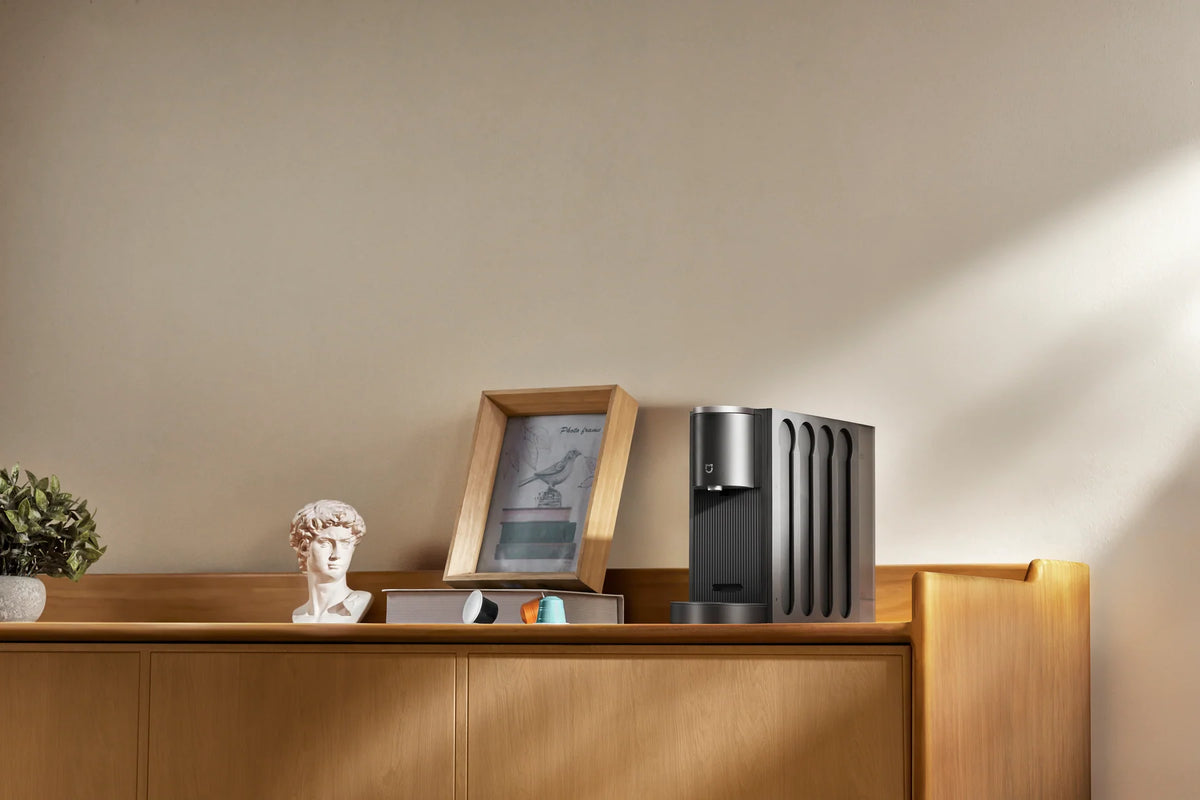 Smalle Xiaomi Mijia Capsule Coffee Machine tussen fotolijstjes op een dressoir